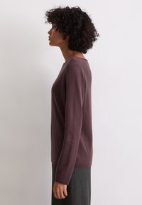 Mauve garš piedurkņu džemperis ar apaļu kakla izgriezumu, izgatavots no mīksta materiāla. Piedāvā šaura piegriezuma dizainu un ribotas aproces, kombinēts ar pelēku svārku.