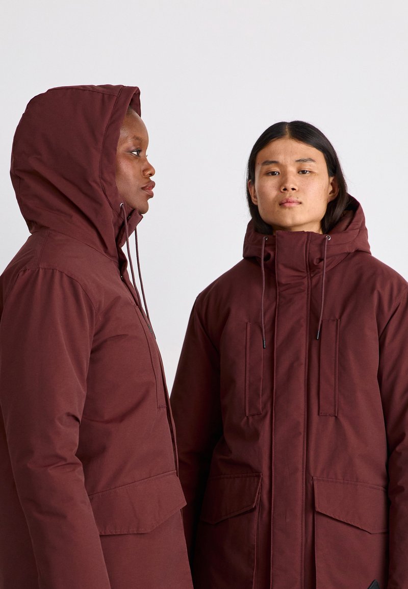 Parker burdeos con capucha, que cuentan con cordones ajustables, dos bolsillos frontales y un acabado de tela texturizada.