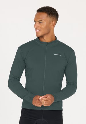 Veste zippée vert foncé avec manches longues, matière légère et texture lisse. Présente un col montant et un branding minimal.