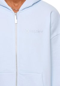 Helles blaues Zip-Hoodie aus weichem Stoff, mit einer Vordertasche und gesticktem "Dropsize"-Logo auf der linken Brust. Silberner Reißverschluss.