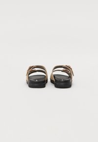 Brune og sorte sandaler med en tekstureret overflade, der har to justerbare stropper og en flad sål. Enkel design med minimal udsmykning.