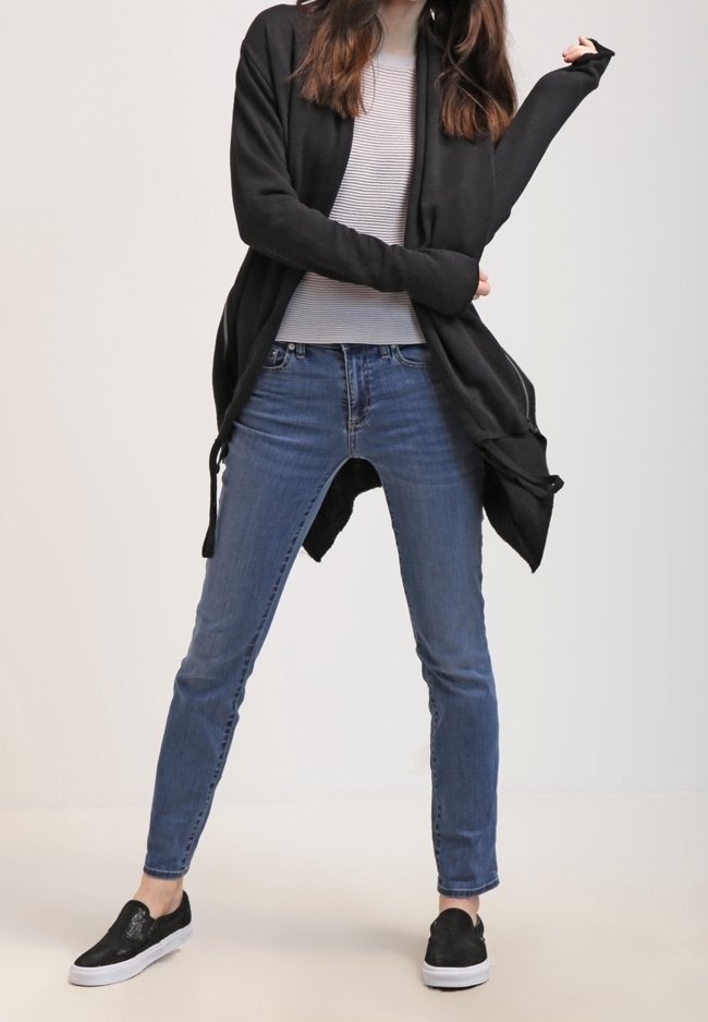 Černý pletený kardigan s otevřeným předním dílem, dlouhými rukávy; pod ním šedý pruhovaný top s dlouhými rukávy, modré úzké džíny, černé boty na slip.