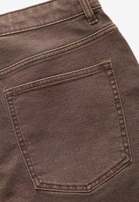 Țesătură de denim de culoare maronie, cu un singur buzunar pe spate, având o cusătură contrastantă și un finisaj texturat. Forma buzunarului este rectangulară, cu colțuri rotunjite.
