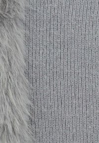 Tessuto grigio lavorato a maglia con costine verticali, caratterizzato da un bordo di morbida pelliccia grigia soffice su un lato. La consistenza è densa e accogliente.