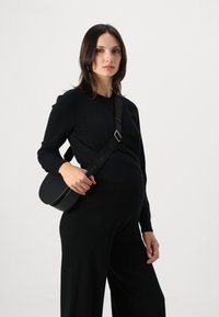 Black leather crossbody bag with a circular shape, featuring a wide adjustable strap and a subtle embossed logo. Smooth texture and minimalist design.
