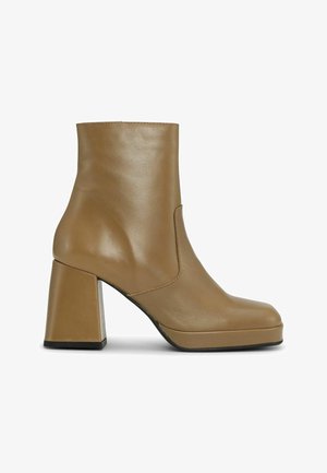 Cizmă de gleznă din piele tan, cu toc pătrat, vârf rotund, design fără cusături și detalii subtile de cusătură de-a lungul marginilor.