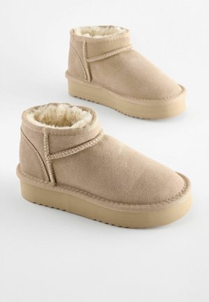 Beige kulkšnai batai, pagaminti iš zomšos, su minkšta dirbtinės kailio pamušalu, su apvalia nosimi, plokščiu guminio pado ir siūlėmis dekoruotais akcentais.