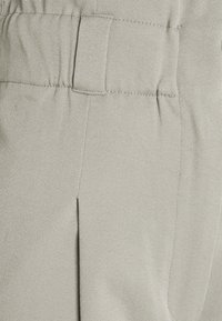 Pantalon gris clair en tissu texturé, avec un devant plat, une taille élastique et des plis latéraux pour un look ajusté.