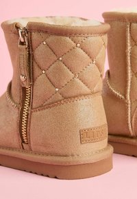 Rudos, pasiūtos kulkšninių botai su šoniniu užtrauktuku, žėrinti tekstūra, puošmenos ir minkštas vidinis pamušalas. Guma sukibimo padas ir prekinis ženklas.