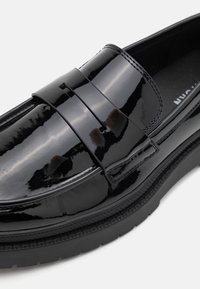 Schwarze Lacklederschuhe mit einer glatten, glänzenden Oberfläche, die einen paddelartigen Riemen über dem Rist und eine strukturierte Gummi-Außensohle aufweisen.