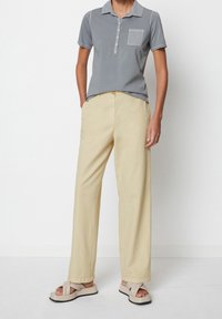 Grå kortärmad polo med krage och bröstficka i kombination med löst sittande ljusbeiga byxor och beiga sandaler.