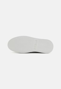 Suela de un zapato negro con una suela de goma blanca y texturizada que presenta el nombre de la marca "FURLA" grabado en el centro.