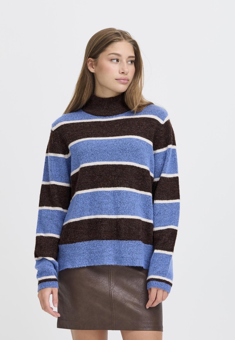 Maglione a strisce blu, marroni e bianche con un collo alto e maniche lunghe; realizzato in un morbido tessuto testurizzato. Abbinato a una gonna in cuoio marrone.