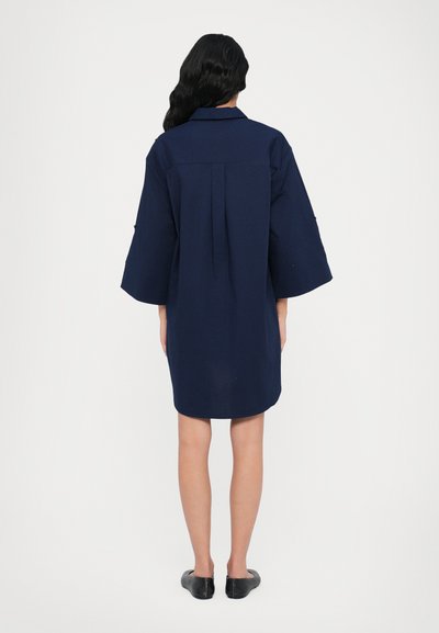 Vestito blu navy con scollo a collare, ampie maniche 3/4 e piega sul retro. Il tessuto sembra liscio con un orlo corto e arrotondato.