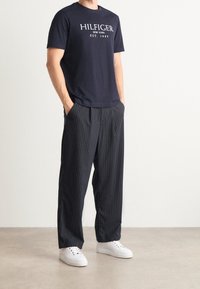 Navy cotton T-shirt with "HILFIGER" print paired with dark striped wide-leg trousers. White sneakers complete the outfit.