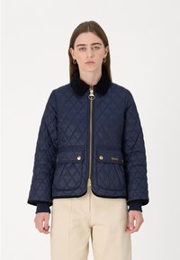 Navy quilted jacket with a zip front, faux fur collar, two front pockets, and gold hardware accents. Features ribbed cuffs and hem.