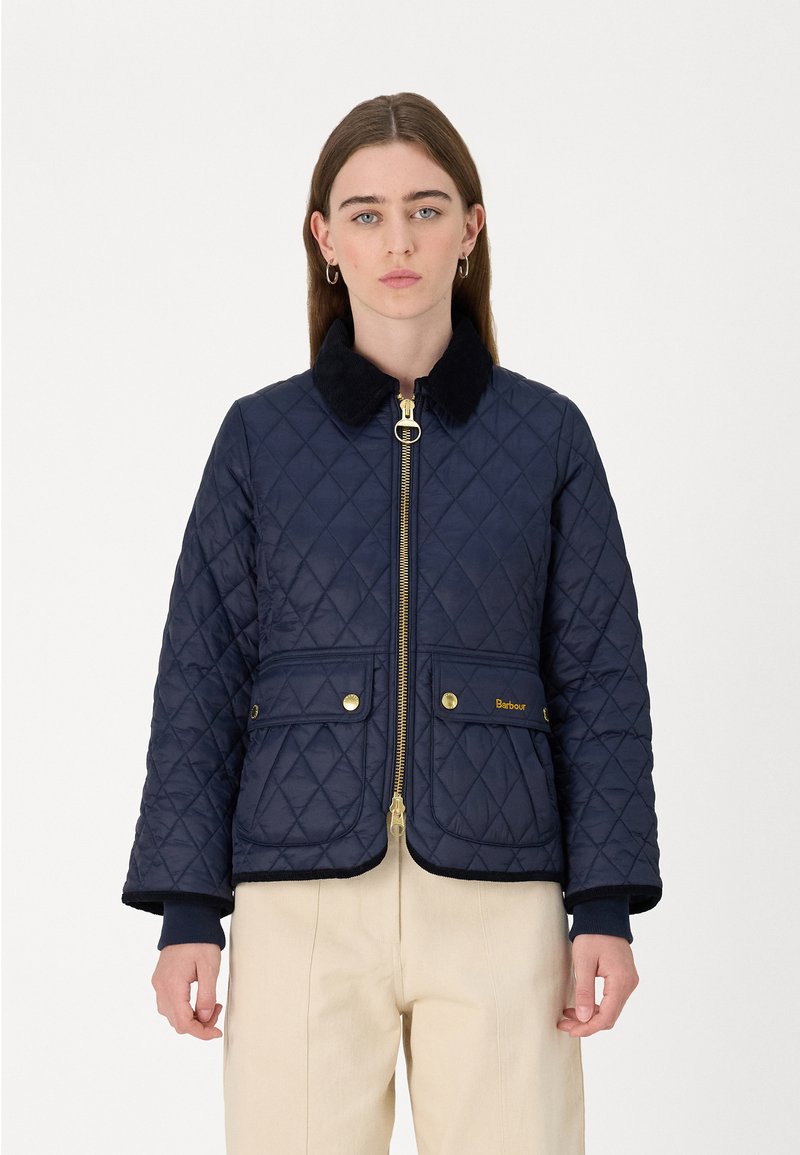 Navy quilted jacket with a zip front, faux fur collar, two front pockets, and gold hardware accents. Features ribbed cuffs and hem.