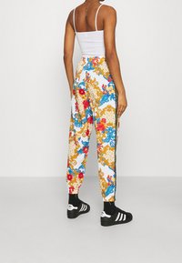 Färgglada joggers med ett blommigt och mönstrat design, med en vit bakgrund, elastisk midja och svarta sidostreck.