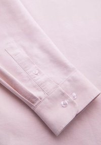 Lichtroze shirtmouw met een geknoopte manchet, voorzien van twee heldere knopen en een gladde textuur, met nadruk op een eenvoudig, op maat gemaakt ontwerp.