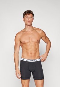 Boxers ajustados de algodón negro con un logo blanco de Nike en la cinturilla. La tela parece suave, ajustada y tiene piernas cortas.