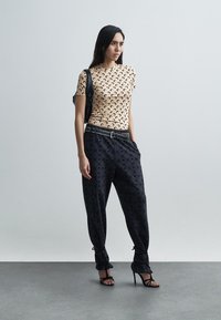 Beżowy krótki top z wzorem księżyca w kształcie sierpa, w połączeniu z czarnymi spodniami w wzory oraz czarnymi sandałami na wysokim obcasie z paskami. Czarna torebka.