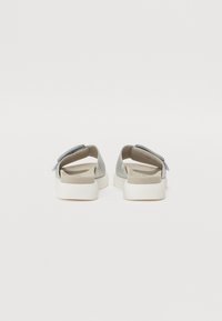Bottines grises sans lacets avec une tige en cuir lisse, une semelle intérieure rembourrée et une semelle en caoutchouc blanc ; elles sont dotées d'une sangle en velcro pour l'ajustement.