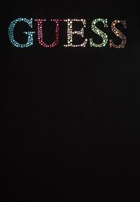 Camiseta negra con la palabra "GUESS" en coloridos cristales brillantes. El texto está centrado, en negrita y brilla con tonos variados.