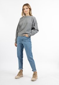 Felpa grigia in cotone con collo rotondo, abbinata a jeans azzurri chiari e stivaletti beige con lacci e suole testurizzate.