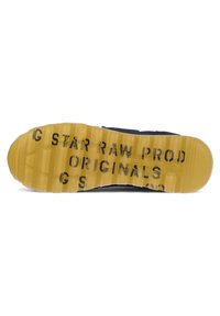 Podešev boty s žlutým gumovým základem a drážkami, černý potisk s textem "G STAR RAW PROD ORIGINALS" a vzorovaná textura.