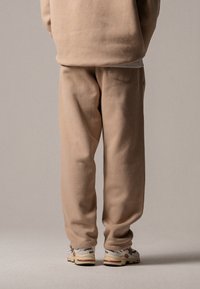 Beige joggebukser laget av fleece-materiale med en avslappet passform, som har en baklomme og brukes med kremhvite og grå sneakers.
