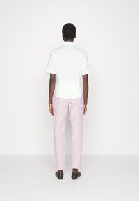 Vit kortärmad skjorta, rosa byxor och svarta skor. Släta tyger med en figurnära silhuett; enkel design utan synliga mönster eller utsmyckningar.