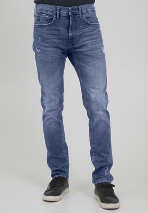 Blå denimjeans med slim fit, med subtil blekning, slitte detaljer og fem lommer. Kombinert med svarte sneakers.