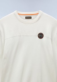 Sweatshirt blanc avec une finition texturée, mettant en avant une nuance orange au col et un patch logo rond sur la poitrine.