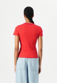 Haut à manches courtes rouge et rose à rayures, avec une coupe ajustée, une texture côtelée et un col rond. Associé à un pantalon en denim large de couleur bleu clair.