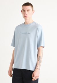 Light blue cotton t-shirt with a crew neck and short sleeves. Features understated "Calvin Klein" embroidered logo on the chest.