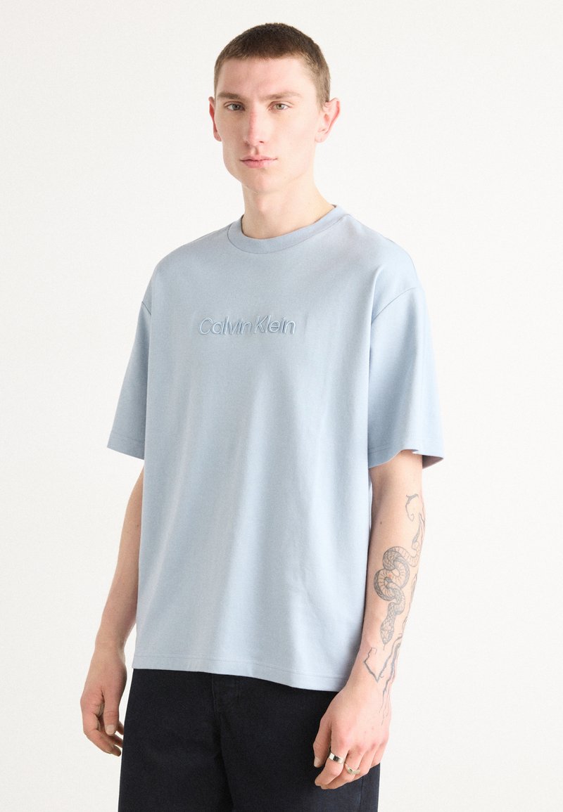 Light blue cotton t-shirt with a crew neck and short sleeves. Features understated "Calvin Klein" embroidered logo on the chest.