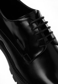 Scarpe in pelle nera con un design elegante, punta tonda e sei paia di lacci neri. Texture liscia con cuciture a contrasto e dettagli laterali.
