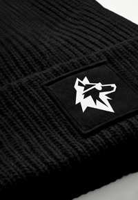 Black knitted beanie featuring a textured pattern and a rectangular black patch with a white wolf graphic design.