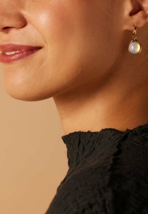 Gold-tone drop earrings feature a teardrop moonstone with a smooth, iridescent surface. Pairing accents with textured black fabric top.