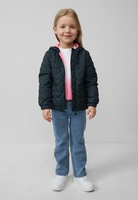 Gequilte donkergroene jas met een roze capuchon, gecombineerd met een witte shirt en lichtblauwe jeans, afgewerkt met witte sneakers. Gladde textuur.