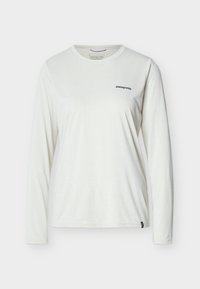 Λευκό γυναικείο μπλουζάκι Patagonia με μακριά μανίκια, στρογγυλή λαιμόκοψη και μικρό μαύρο λογότυπο στο αριστερό μέρος του στήθους, σε απλό φόντο.