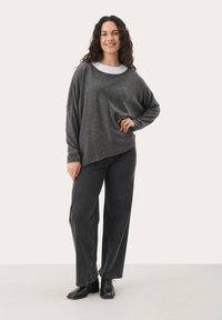 Oversized gray knit sweater with a wide neckline, layered over a white shirt, paired with loose black jeans and black ankle boots.