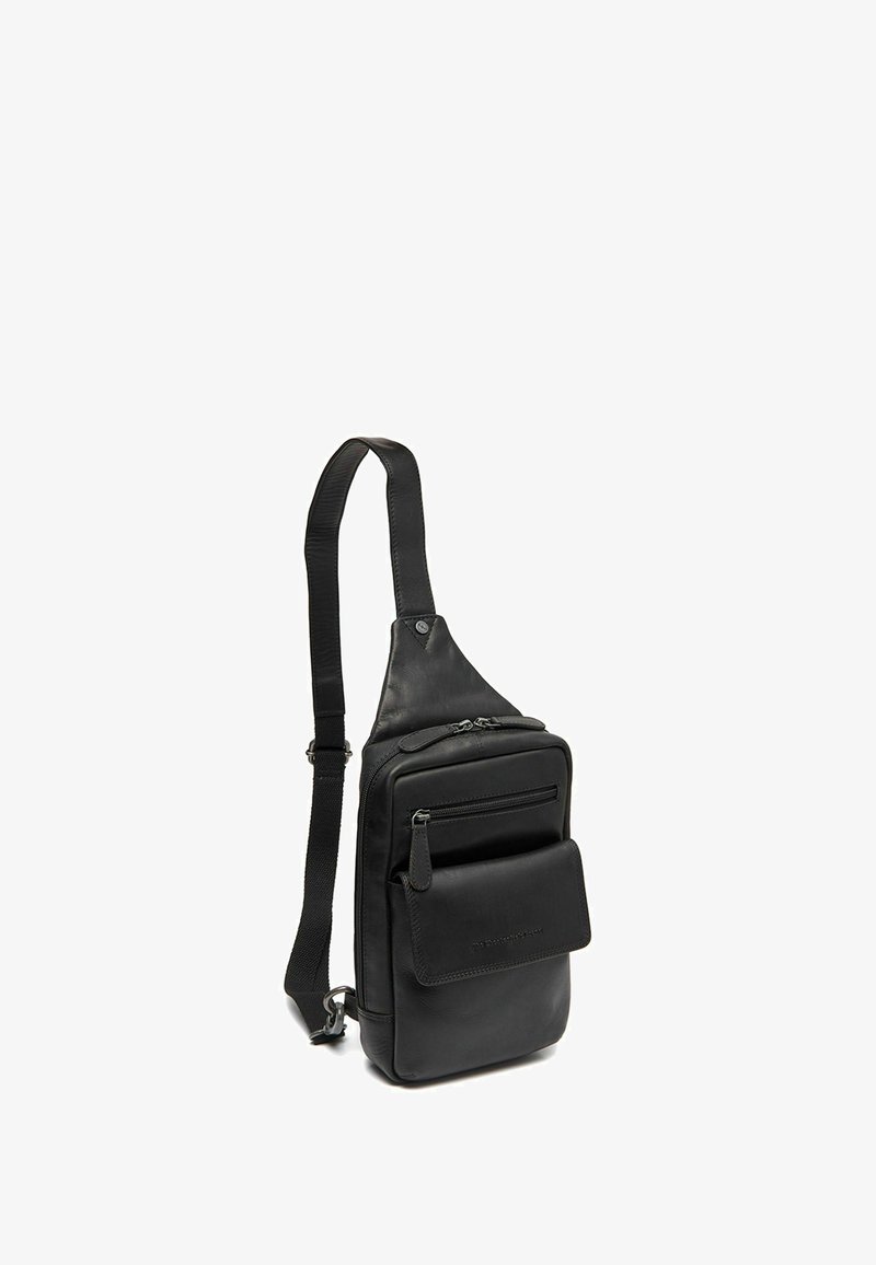 Sac à dos en cuir noir avec une bandoulière réglable, compartiment principal zippé et poche avant. Texture lisse avec des accents matériels minimalistes.