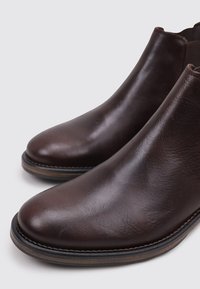 Botas de tobillo de cuero marrón con un acabado suave, punta redonda, tacón bajo apilado y un detalle de pespunte contrastante en la suela.