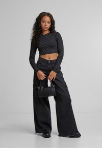 Fekete crop top geometrikus mintával, párosítva magas derékú fekete bővülő cargo nadrággal. Kézben tart egy kis fekete táskát ezüst részletekkel.