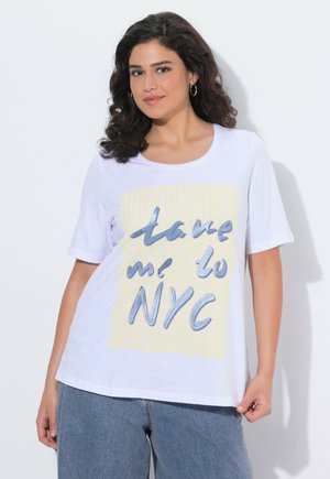 Donna con capelli ricci e scuri che indossa orecchini a cerchio dorati, una maglietta bianca con strisce gialle e la scritta "portami a New York", e jeans di denim blu.