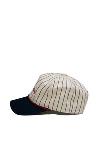 Kappe laget av kremfarget stoff med marineblå striper, marineblå skjerm og et rødt accentbånd. Har broderte bokstaver på forsiden, strukturert design.