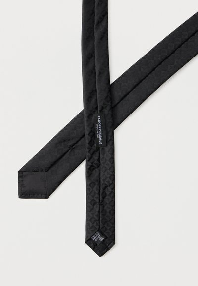 Cravate en soie noire de créateur avec un motif géométrique subtil, présentant l'étiquette de la marque "Emporio Armani Made in Italy" sur le revers.
