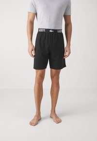 Shorts noirs avec ceinture élastique arborant le logo "LACOSTE", fabriqués en tissu doux et dotés d'une coupe décontractée.