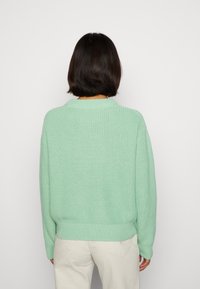 Maglione lavorato a maglia verde menta con una vestibilità rilassata, texture a coste e colletto a girocollo. Abbinato a pantaloni chiari.